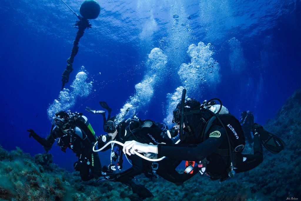 Gruppo di subacquei durante un addestramento di emergenza in immersione, con attrezzatura completa e cime di ormeggio in evidenza.