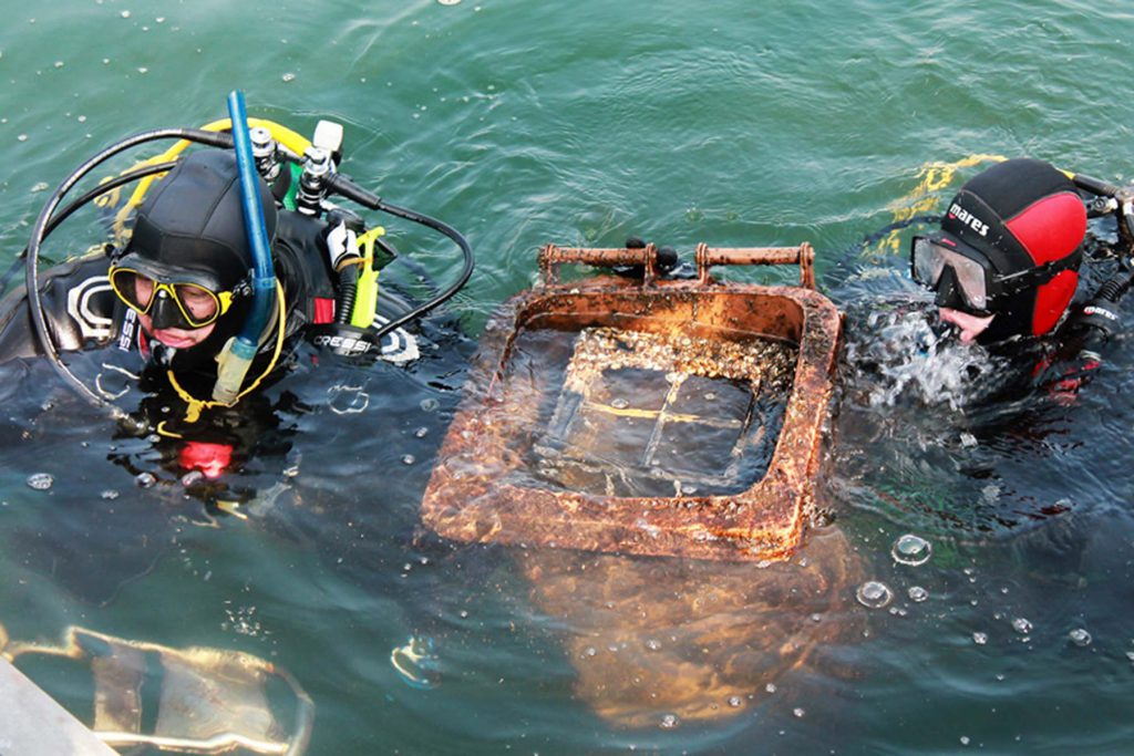 Due subacquei in acqua con un oggetto arrugginito